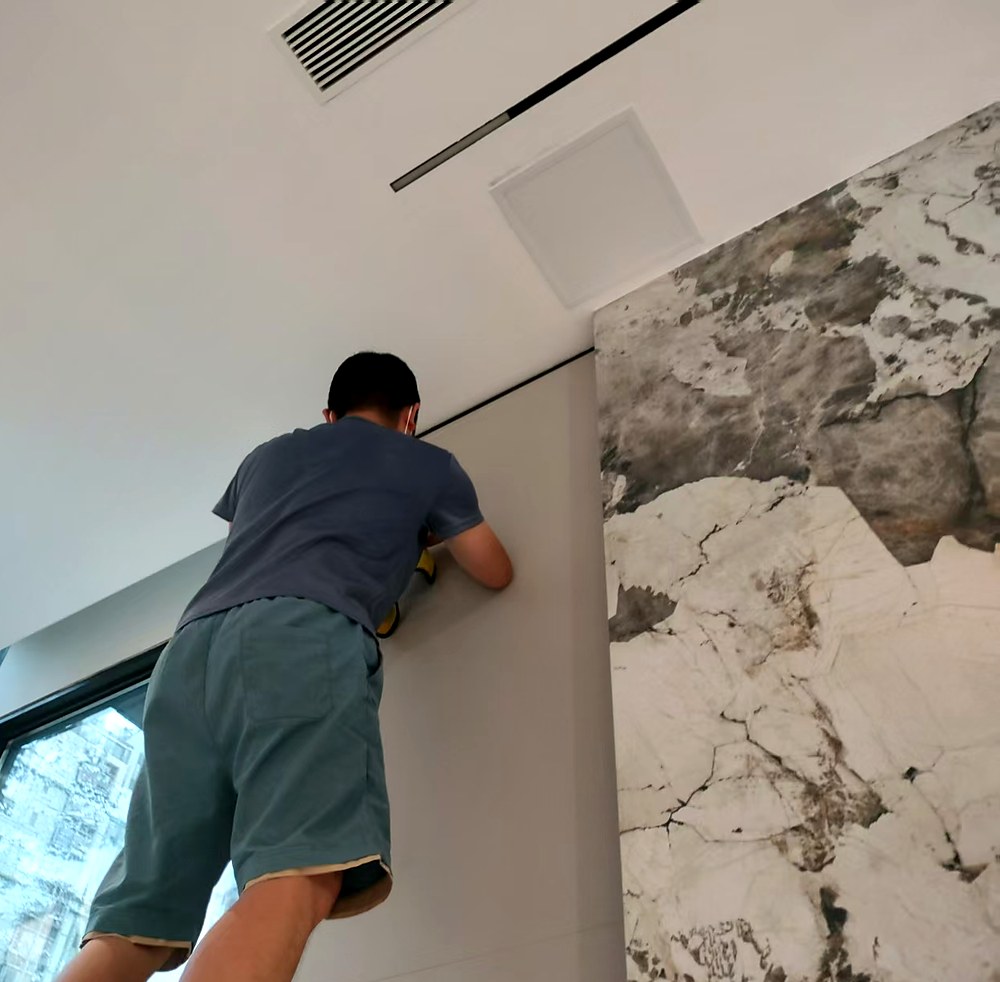 深圳宝安深业新岸线旧改新开荒，师傅在人字梯上清理挑空区高处墙面，右侧为大理石背景墙